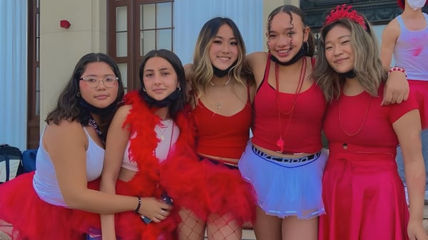 Eine Gruppe junger Frauen in roten Outfits posiert vor einem Gebäude auf dem Campus des Alameda Unified School District.