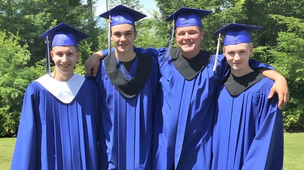 Vier Schüler in blauen Abschlusskleidern stehen auf dem Gelände der Alberni District Secondary School in einem bewaldeten Bereich.