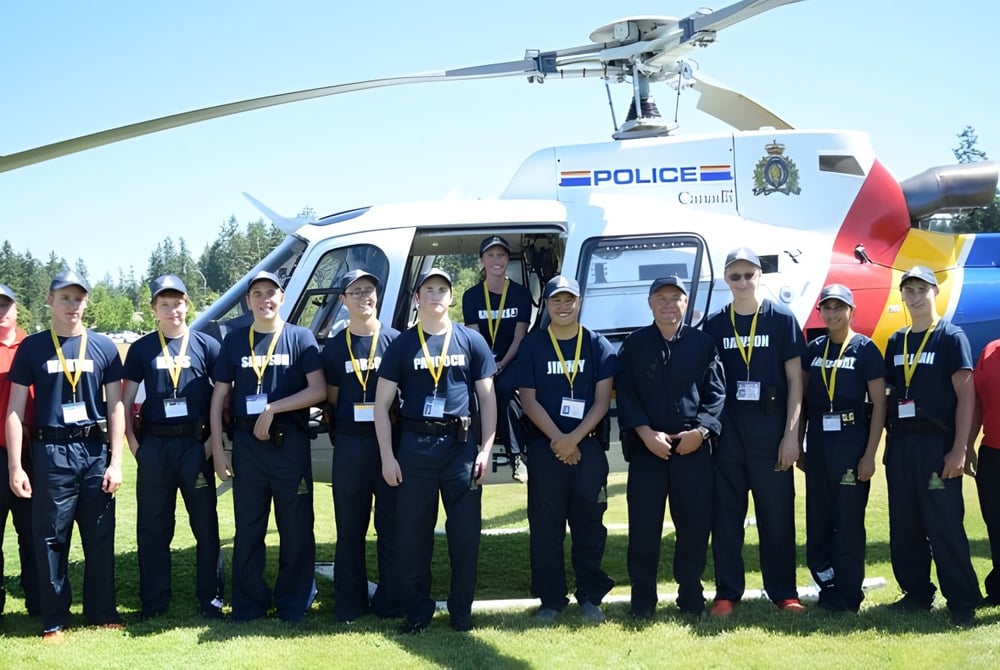 Eine Gruppe Polizeibeamter steht vor einem Polizeihubschrauber auf einem Grasfeld auf dem Gelände der Alberni District Secondary School.
