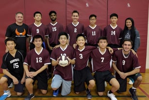 Die Volleyballmannschaft des Albert Campbell Collegiate Institute posiert gemeinsam in der Sporthalle vor einer roten Wand.