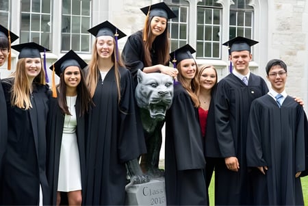 Eine Gruppe von Absolventinnen und Absolventen sowie ein Hund posieren vor einem Gebäude auf dem Campus des Albert College.