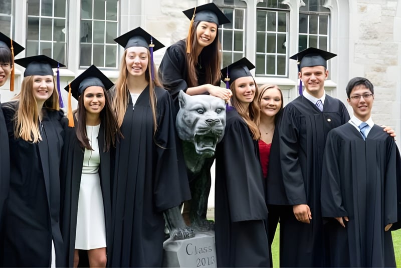 Eine Gruppe von Absolventinnen und Absolventen sowie ein Hund posieren vor einem Gebäude auf dem Campus des Albert College.