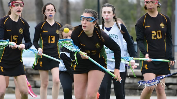 Eine Gruppe Schülerinnen des Albert College steht mit Lacrosse-Schlägern auf einem Spielfeld mit Bäumen im Hintergrund.