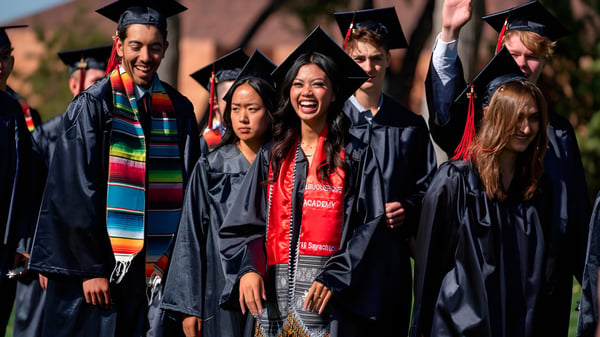 Eine Gruppe von Absolventen steht im Freien in bunter akademischer Kleidung auf dem Campus der Albuquerque Academy.