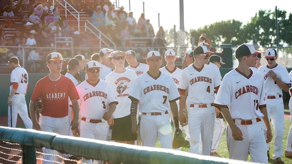 Eine Gruppe von Baseballspielern der Albuquerque Academy steht auf dem Spielfeld mit Zuschauern im Hintergrund.