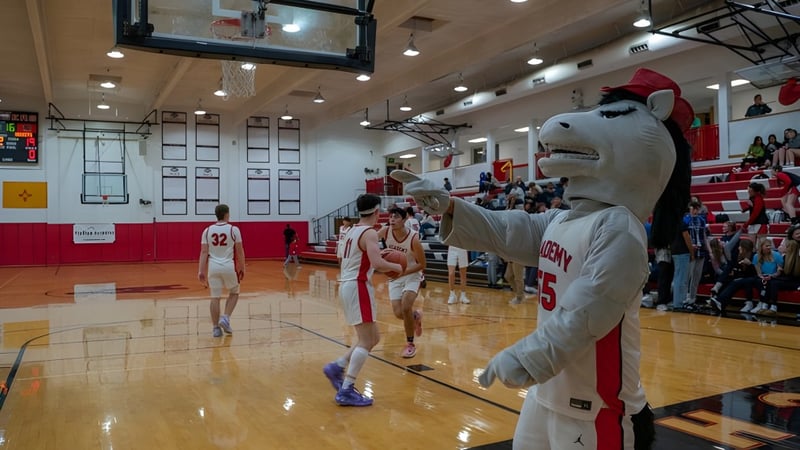 Schüler der Albuquerque Academy spielen Basketball auf dem Schulhof mit Maskottchen und Zuschauern auf den Tribünen.