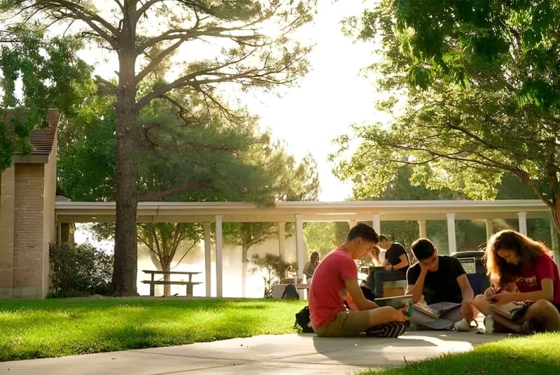 Eine Gruppe Schülerinnen und Schüler der Albuquerque Academy sitzt auf der Wiese in einem von Bäumen gesäumten Außenbereich.