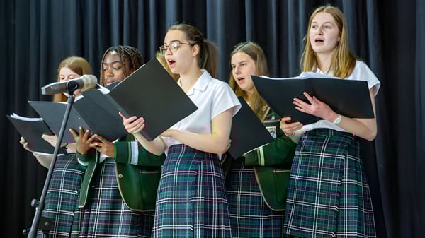 Eine Gruppe Schülerinnen der Albyn School treten mit Schuluniformen und Notenblättern auf einer Bühne auf.