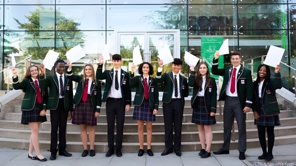 Schüler in Schuluniformen stehen vor einem modernen Glasgebäude auf dem Campus der Albyn School und halten Papiere oder Schilder hoch.