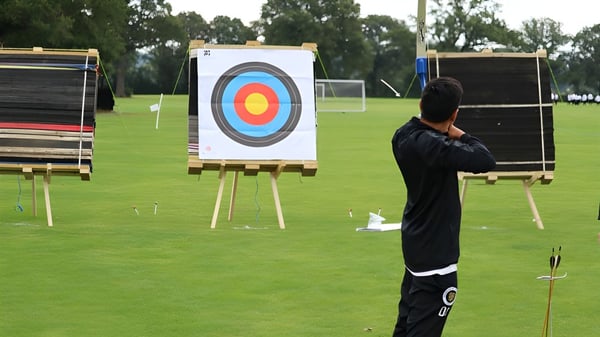 Eine Schülerin oder ein Schüler der Aldenham School steht vor einer Bogenschießscheibe auf einem grasbewachsenen Feld mit Bäumen.