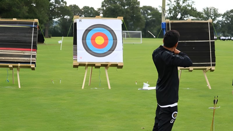 Eine Schülerin oder ein Schüler der Aldenham School steht vor einer Bogenschießscheibe auf einem grasbewachsenen Feld mit Bäumen.