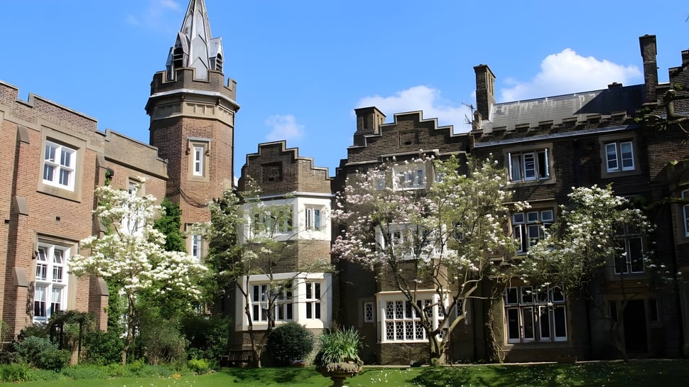 Das historische Backsteingebäude mit einem hohen Turm steht auf dem Gelände der Aldenham School umgeben von grünen Bäumen und blühender Vegetation.