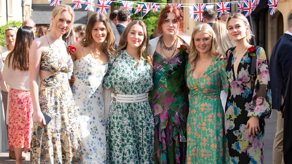 Eine Gruppe Schülerinnen der Aldenham School steht in bunten Kleidern vor einer mit Union Jack Flaggen geschmückten Straße.