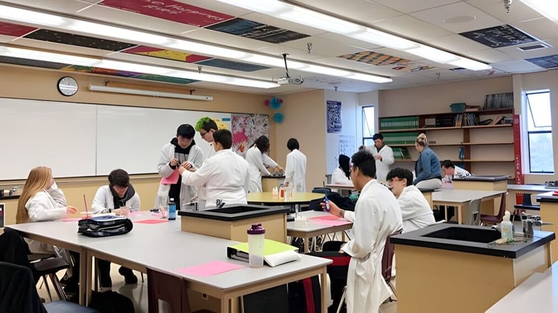 Schüler in Laborkitteln arbeiten im Klassenraum der Aldergrove Community Secondary School an verschiedenen Stationen.