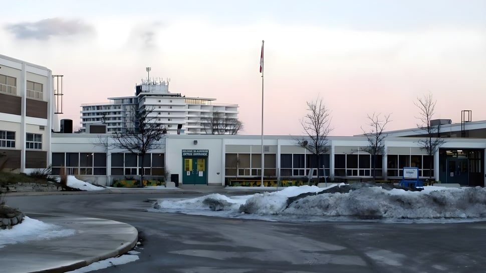 Das mehrstöckige Gebäude mit einem hohen Turm der Aldershot High School ist von einem verschneiten Parkplatz und bewölktem Himmel umgeben.