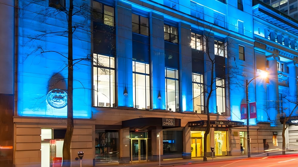 Das mehrstöckige Gebäude der Alexander Academy ist nachts mit erleuchteten Fenstern und Bäumen davor zu sehen.