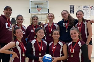 Eine Gruppe junger weiblicher Athletinnen steht in der Sporthalle der Alexander Mackenzie High School vor einem Basketballkorb.