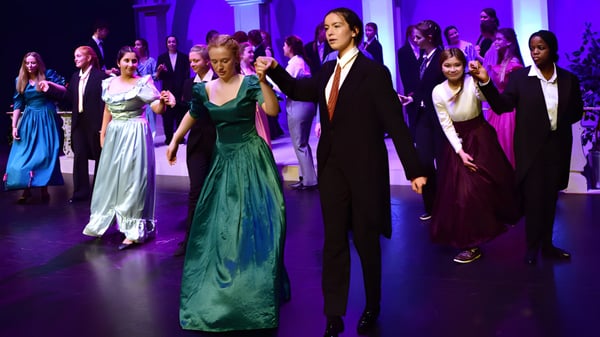 Eine Gruppe elegant gekleideter Schülerinnen und Schüler von Alexandra College bei einer festlichen Veranstaltung unter violetter Beleuchtung.