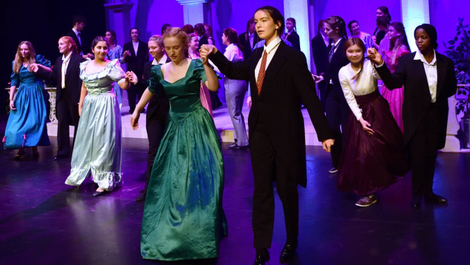 Eine Gruppe formal gekleideter Personen steht auf der Bühne bei einer Veranstaltung des Alexandra College mit purpurnem Bühnenlicht.