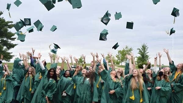 Absolventen der Alexandra Hills State High School werfen ihre Hüte in die Luft vor Bäumen und bewölktem Himmel.