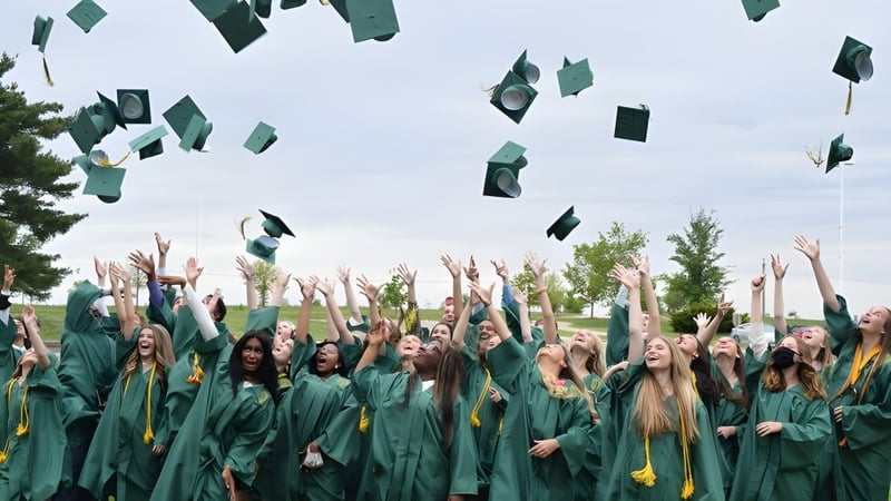 Absolventen der Alexandra Hills State High School werfen ihre Hüte in die Luft vor Bäumen und bewölktem Himmel.