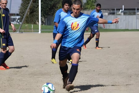 Eine Gruppe Schüler spielt Fußball auf dem Sportfeld des Alfriston College, während ein Spieler den Ball am Fuß führt.