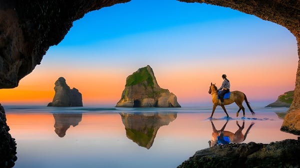 Eine Person auf einem Pferd steht am Strand vor Felsen während des Sonnenuntergangs nahe dem Alfriston College.