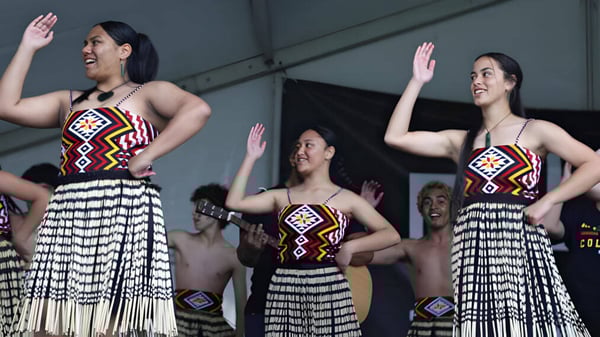 Drei Frauen führen auf der Bühne vor dem Publikum des Alfriston College einen traditionellen Tanz in farbenfrohen Kleidern auf.