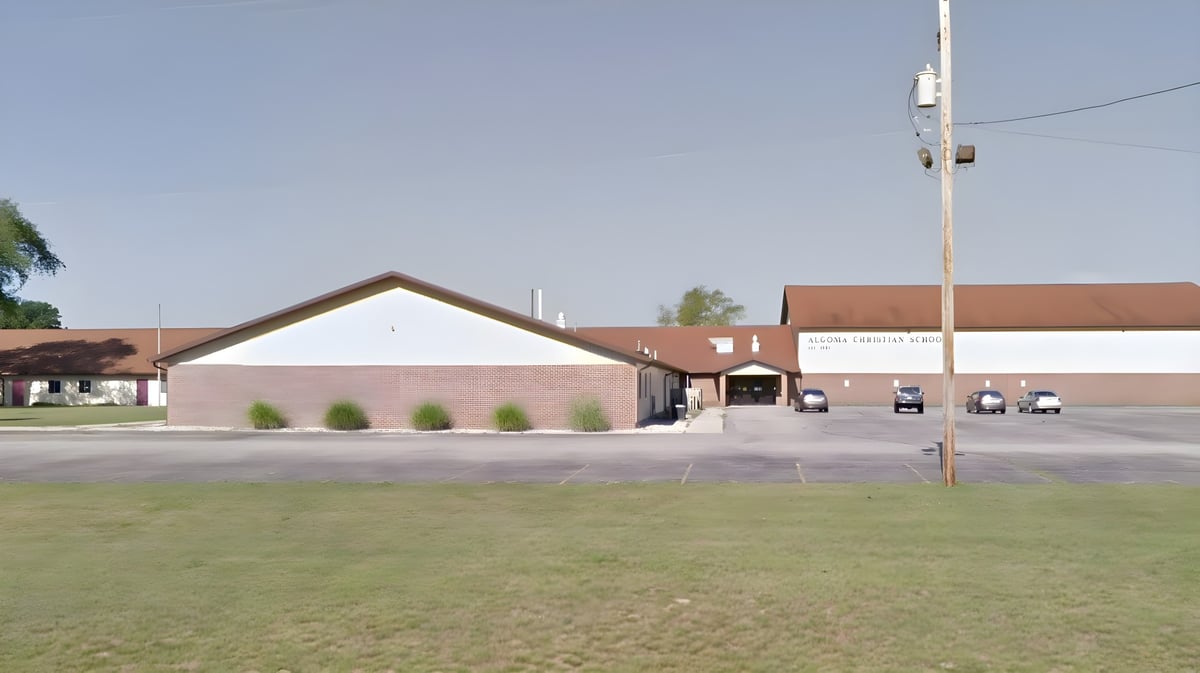 Das große Backsteingebäude mit Spitzdach auf dem Campus der Algoma Christian High School ist von einer Wiese und einigen Bäumen umgeben.