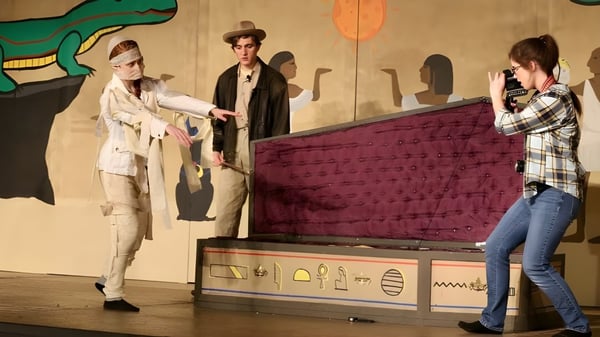 Drei Personen stehen vor einer bunten Kunstwand mit einem großen grünen Dinosaurier auf dem Campus der Algoma Christian High School.