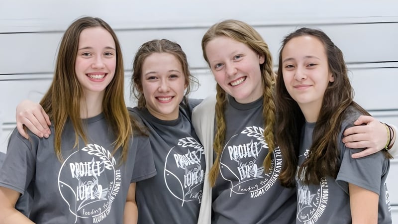 Vier Schülerinnen der Algoma Christian High School stehen zusammen vor einem neutralen Hintergrund und lächeln.