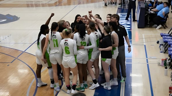 Eine Gruppe weiblicher Basketballspielerinnen im Trikot steht auf dem Spielfeld des Algonquin College mit Zuschauern im Hintergrund.