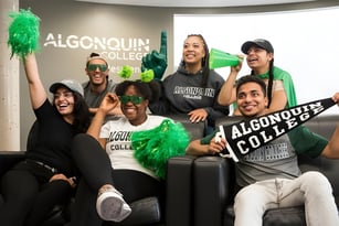 Eine Gruppe Schüler vor dem Algonquin College Schild hält grüne Pompons und posiert gemeinsam.