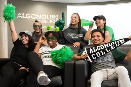 Eine Gruppe Schüler vor dem Algonquin College Schild hält grüne Pompons und posiert gemeinsam.