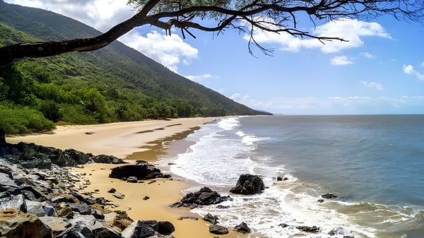 Ein Küstenlandschaft mit Sandstrand, Felsen und grünen Bergen, aufgenommen in der Nähe der All Saints Anglican School.