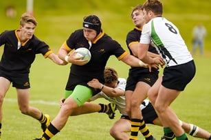 Schüler der All Saints Anglican School spielen ein intensives Rugby-Match auf einem grünen Spielfeld.