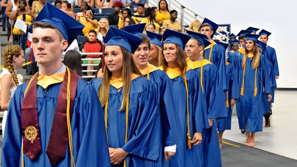 Eine Gruppe Absolventen der All Saints High School in blauen und gelben Talaren steht zusammen vor einer Menschenmenge.