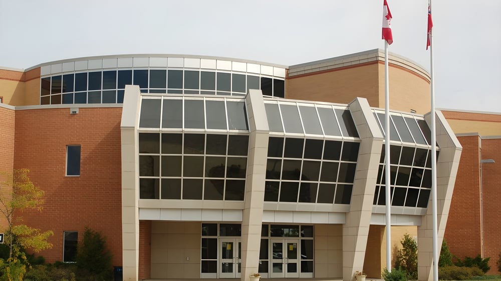 Das moderne mehrstöckige Gebäude der All Saints High School mit einer geschwungenen Glasfassade und einer kanadischen Flagge auf dem Dach.