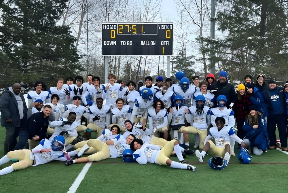 Die Sportmannschaft der All Saints High School in Calgary versammelt sich auf einem schneebedeckten Spielfeld vor der Anzeigetafel.