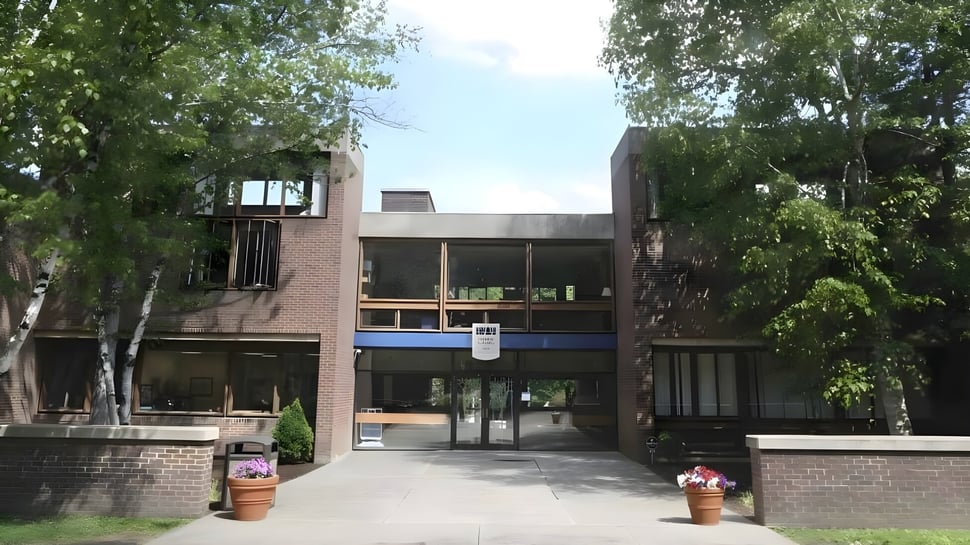 Das moderne Backsteingebäude der Allendale Columbia School mit großen Fenstern und überdachtem Eingang umgeben von Bäumen.