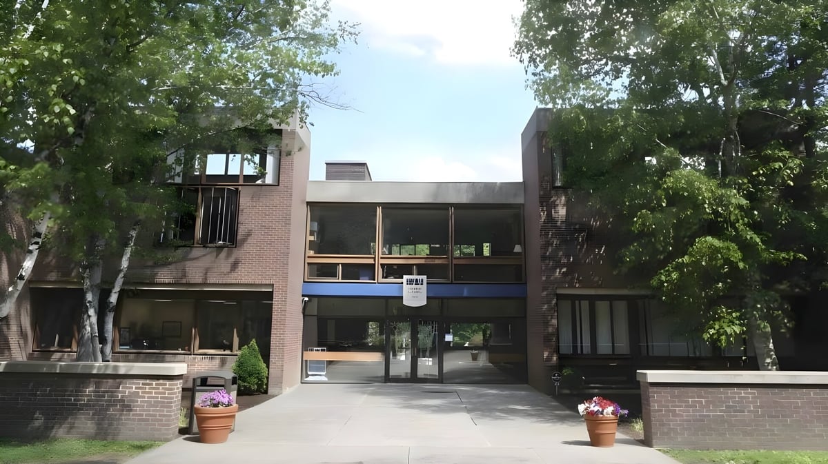 Das moderne Backsteingebäude der Allendale Columbia School mit großen Fenstern und überdachtem Eingang umgeben von Bäumen.