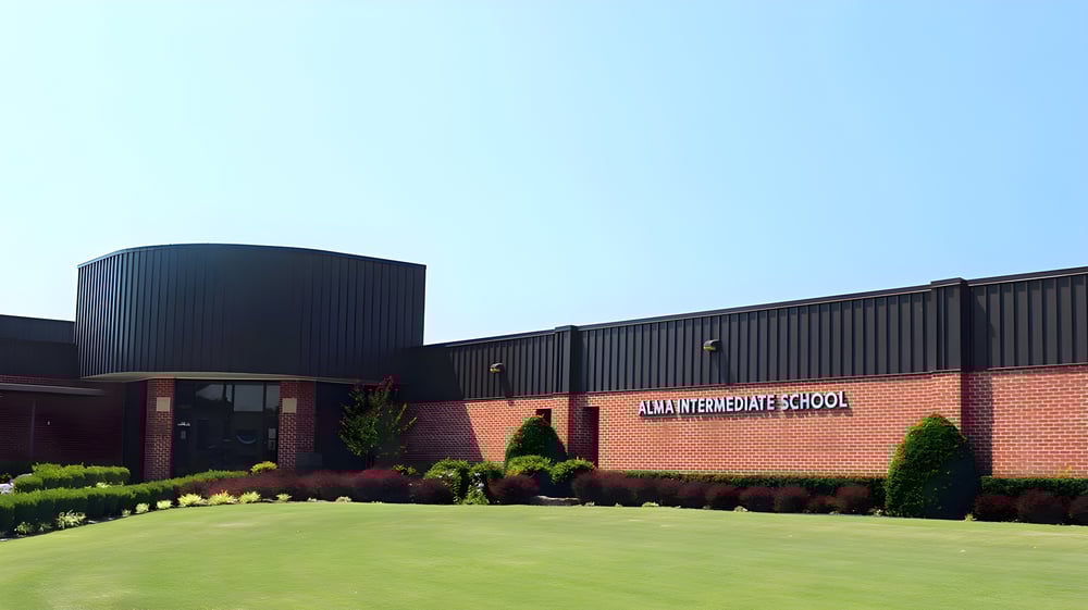 Das moderne Backsteingebäude der Alma High School mit geschwungenem Dach und gepflegtem Außenbereich.