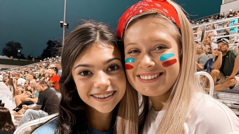Zwei Schülerinnen der Alma High School posieren im voll besetzten Stadion mit zahlreichen Zuschauern im Hintergrund.
