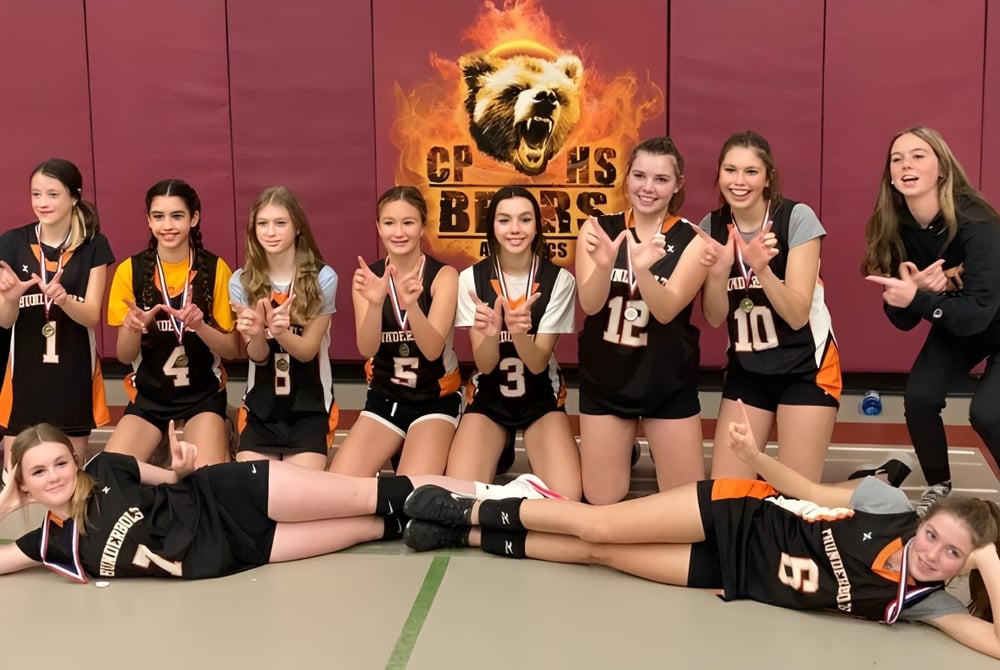 Eine Gruppe weiblicher Volleyballspielerinnen der Almonte & District High School posiert gemeinsam vor einem feurigen Hintergrund.