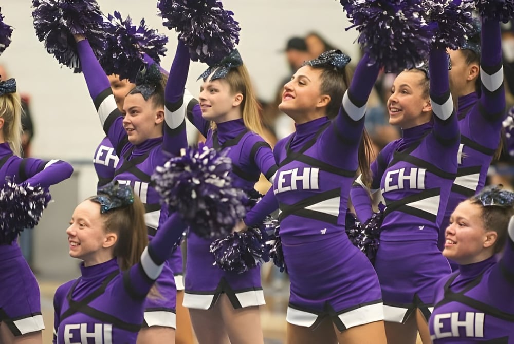 Schülerinnen und Schüler der Alpine School District als Cheerleader in lila Uniformen mit Pompons vor einem Banner mit dem Schriftzug EHI.