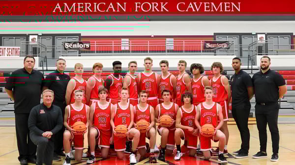 Die Basketballmannschaft des Alpine School District posiert in roten Trikots vor einem Banner mit der Aufschrift American Fork Cavemen.