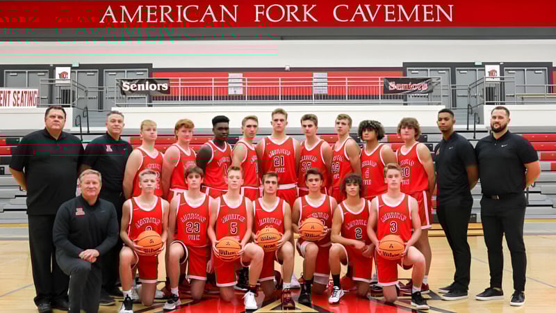 Die Basketballmannschaft des Alpine School District posiert in roten Trikots vor einem Banner mit der Aufschrift American Fork Cavemen.