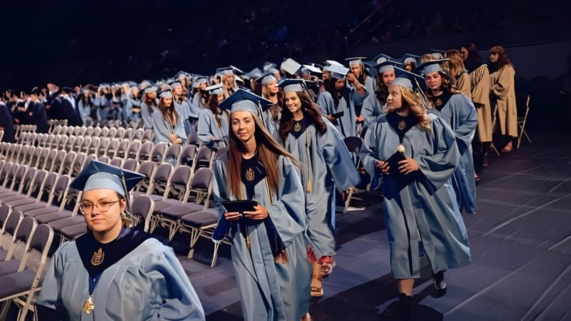 Eine Gruppe von Schülerinnen und Schülern auf dem Campus der Alpine School District tragen graue Roben und Kapuzen und stehen in Reihen vor dunklem Hintergrund.
