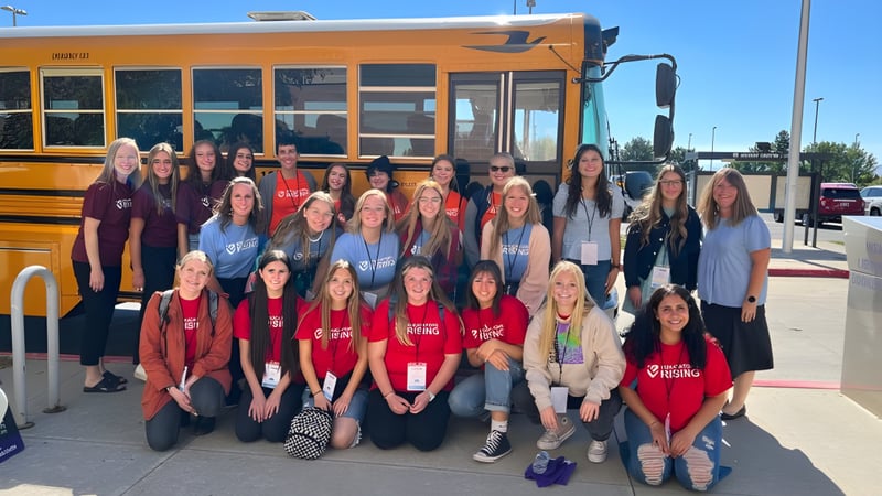 Eine Gruppe Schülerinnen der Alpine School District steht vor einem gelben Schulbus mit blauem Himmel im Hintergrund.