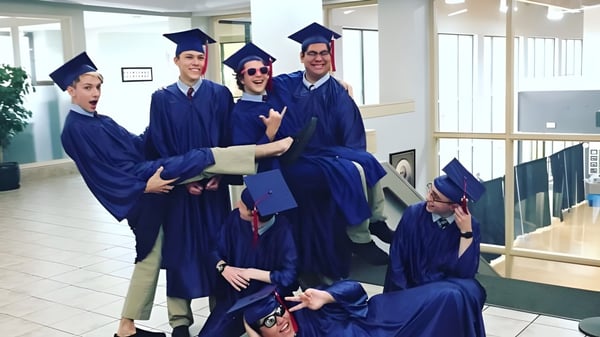 Eine Gruppe von Absolventen der American Heritage Academy steht im Flur mit blauen Talaren und Hüten nach der Abschlussfeier.